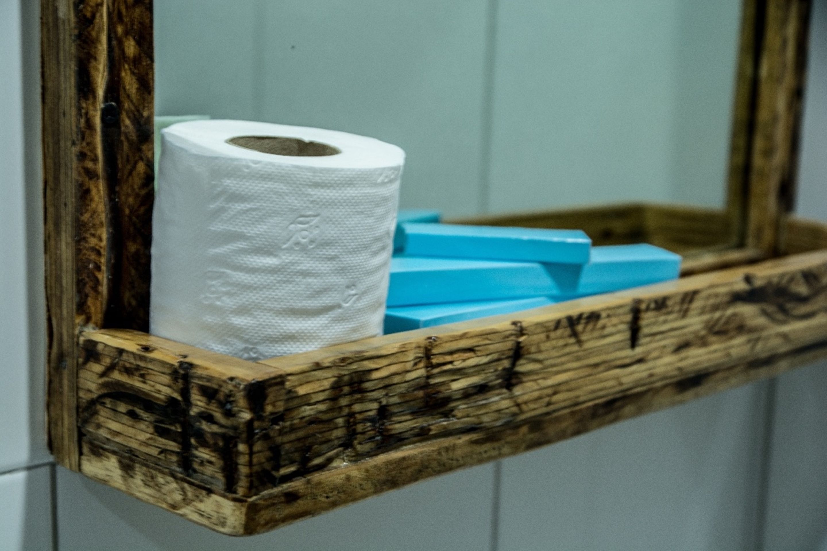 Ein Holzregal mit einer Toilettenpapierrolle und blauen Seifenstücken.