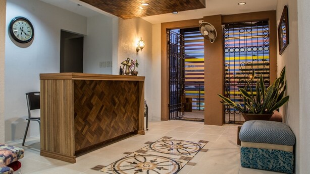 A reception area with a wooden reception desk, a clock, a potted plant, and a patterned floor. - Hotel Avenija (Olongapo)