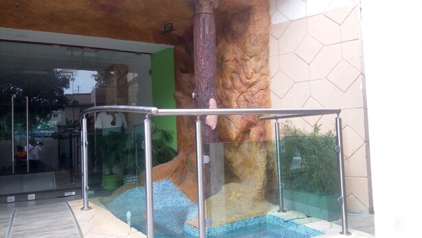 A glass-enclosed entrance with a metal railing, a tiled pool area, and a green wall with a textured design. - Eifell's Hotel's (Abidjan)