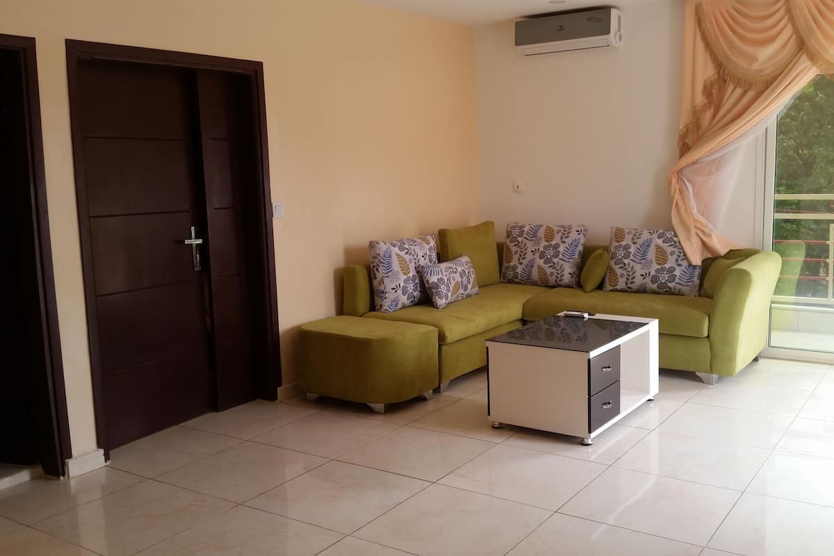 A living room with a green sofa, patterned cushions, a small coffee table, and a sliding glass door leading to a balcony.