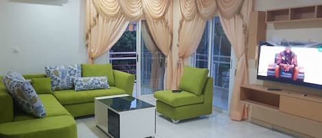 A living room with green sofas, a glass coffee table, and a TV on a wooden stand.