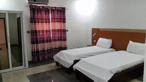 Hotellihuone, jossa on kaksi erillistä sänkyä, puinen pääty, liukuovi ja kuvioitu verho.