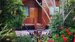 A wooden cabin with a porch, surrounded by lush greenery and flowering plants. - Asya Bungalow (Kemer)