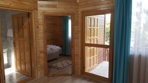 A wooden cabin with a bedroom featuring a bed, a window, and a door leading to an outdoor area. - Asya Bungalow (Kemer)