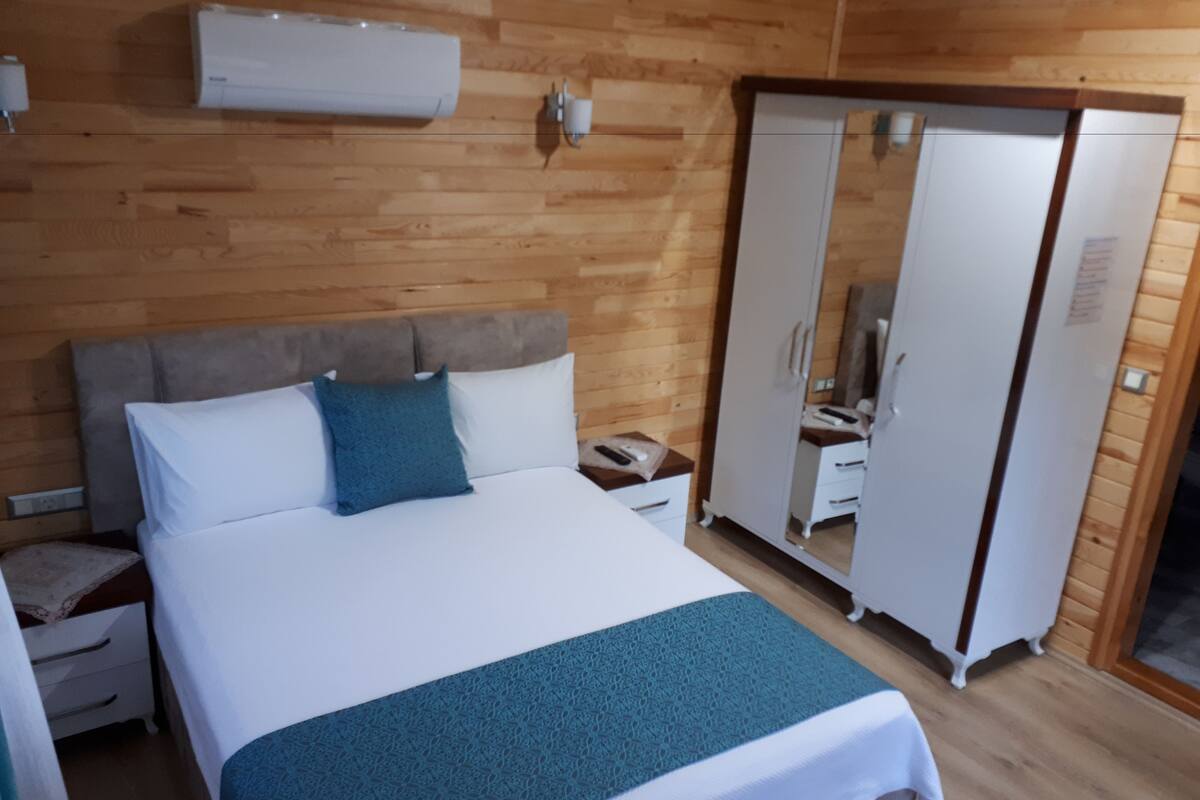 A bedroom with a bed, a nightstand, a wardrobe, and an air conditioning unit on the wall.