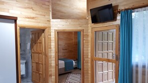 A wooden cabin with a bed, a television, and a bathroom visible through a door. - Asya Bungalow (Kemer)