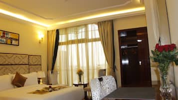 Habitación de hotel con cama, escritorio, silla, un jarrón con flores y ventana con cortinas.