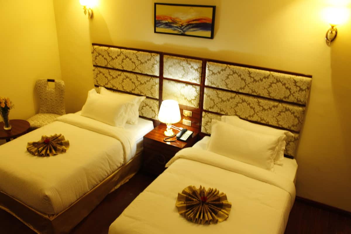 A hotel room with two beds, a nightstand with a lamp, a chair, and a painting on the wall.
