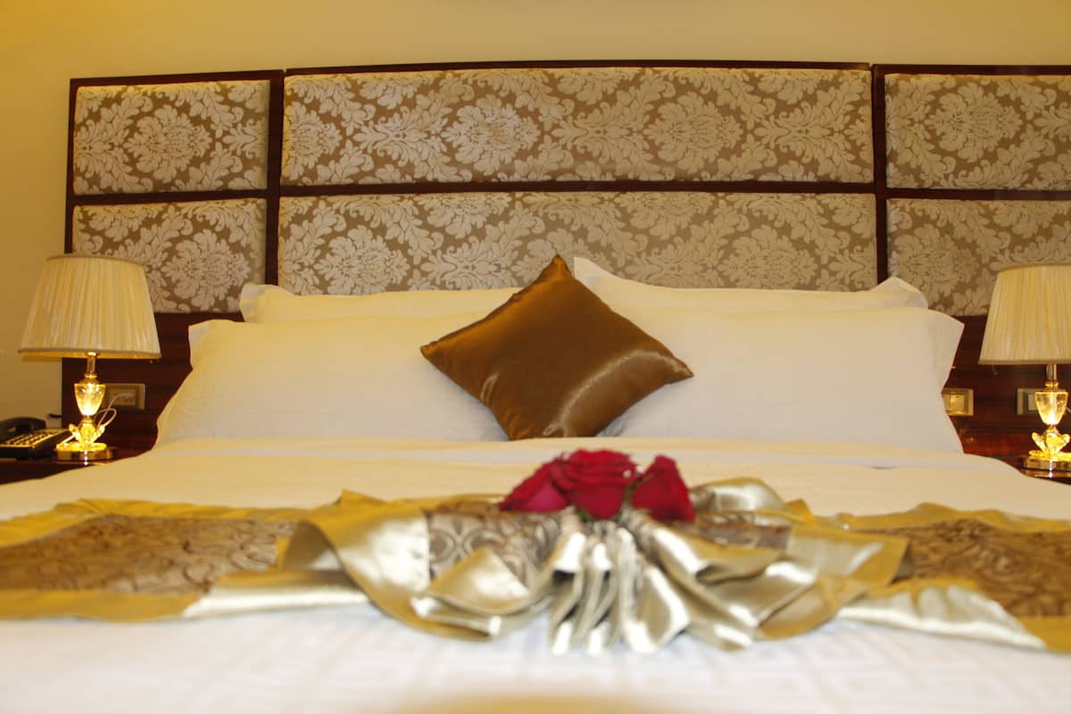 A neatly made bed with a decorative pillow, a bouquet of flowers, and a gold-trimmed bedspread.
