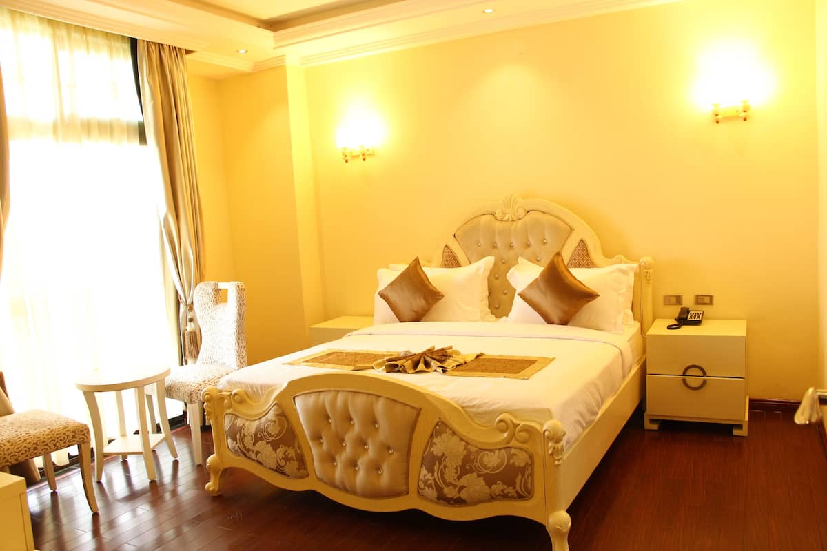 A large bed with a tufted headboard, two bedside tables, a nightstand, and a chair.