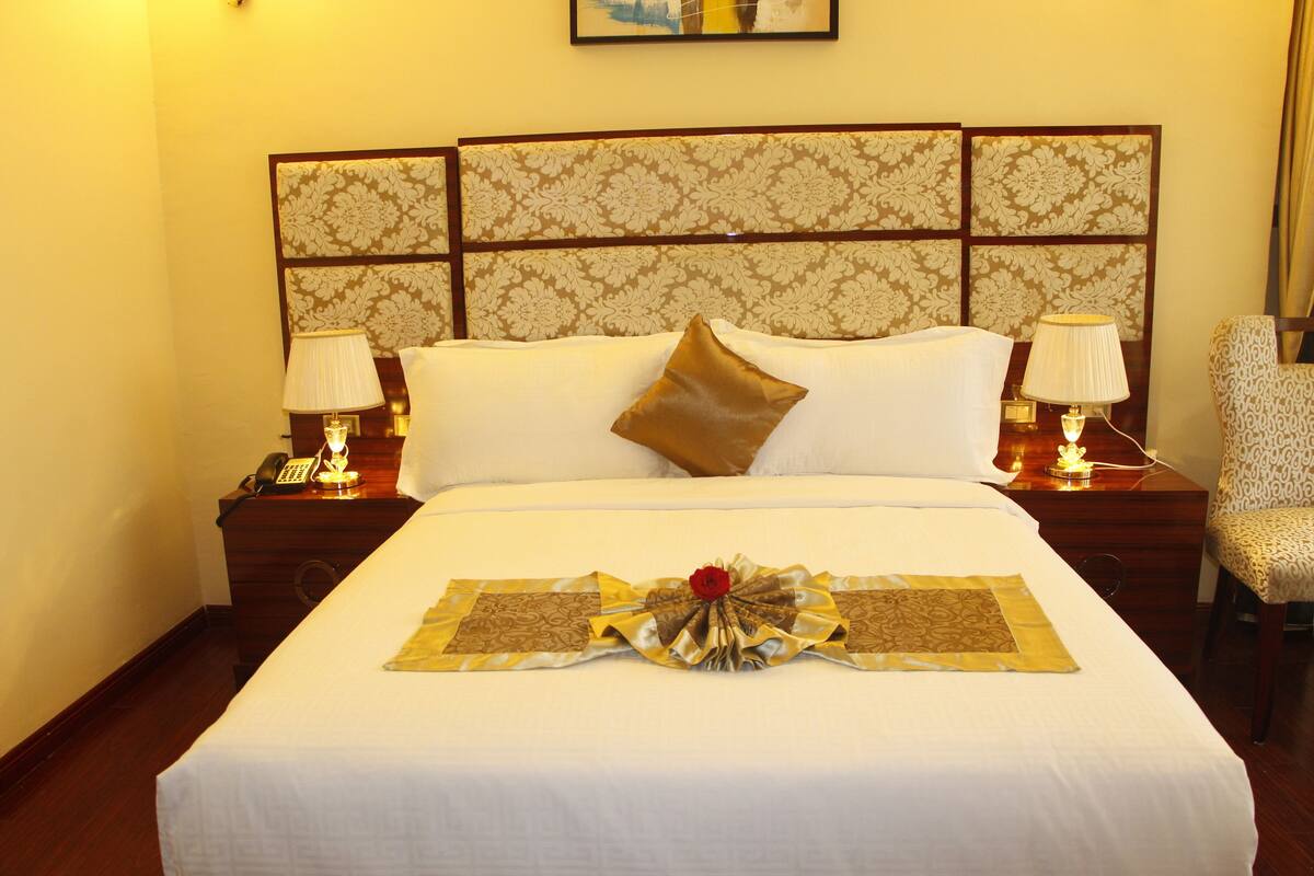 A neatly made bed with a decorative headboard, two bedside lamps, and a chair.