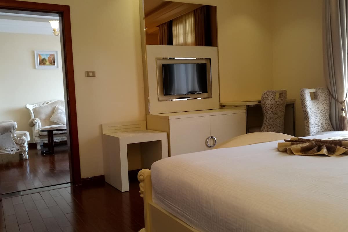 A hotel room with a bed, a TV mounted on the wall, a small bedside table, a chair, and a patterned throw on the bed.