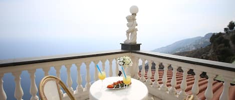 Un balcon avec une table dressée pour deux personnes, une statue et une vue panoramique.