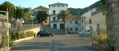 A gated driveway leading to a building with a two-story structure, a palm tree, and parked cars.