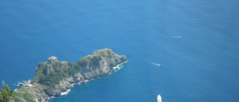 A coastal landscape with a rocky island, a small boat, and a distant building.