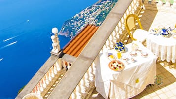 Una terraza con mesa lista para el desayuno, con vista a la costa.