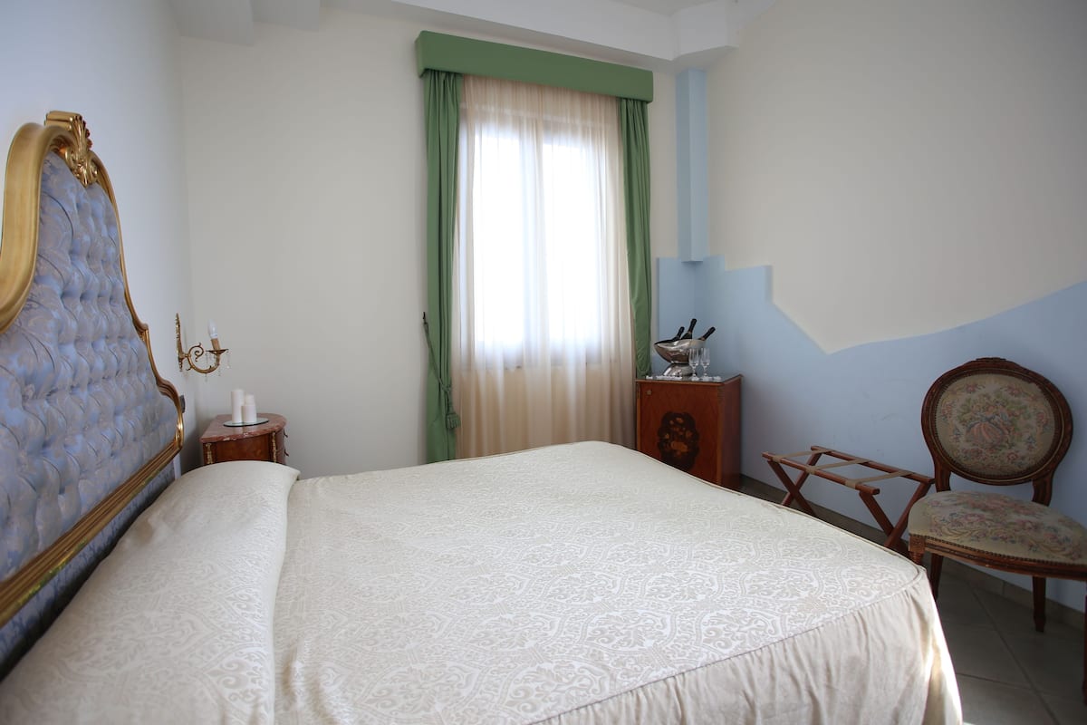 A bedroom with a large bed, a dresser, a chair, and a window with curtains.