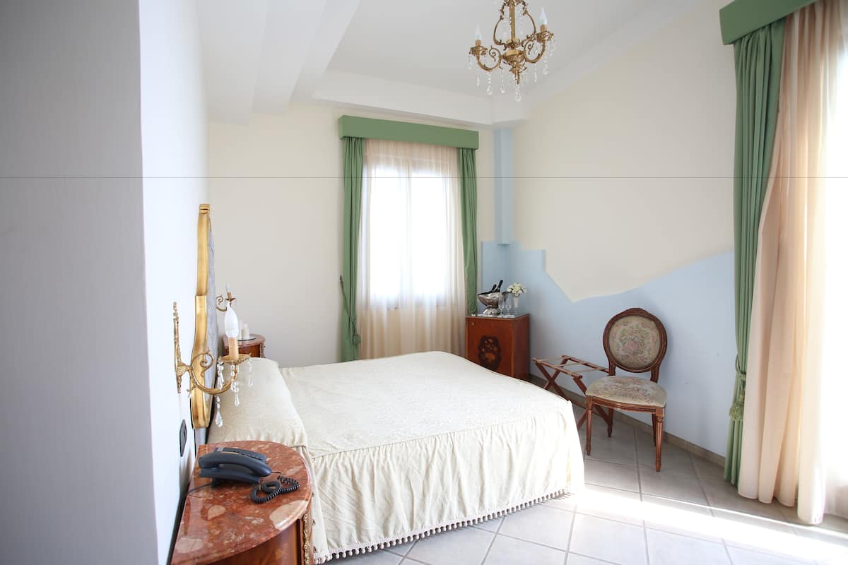 A bedroom with a bed, a chair, a nightstand, a chandelier, and curtains.
