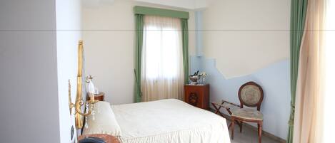 A bedroom with a bed, a chair, a nightstand, a chandelier, and curtains.