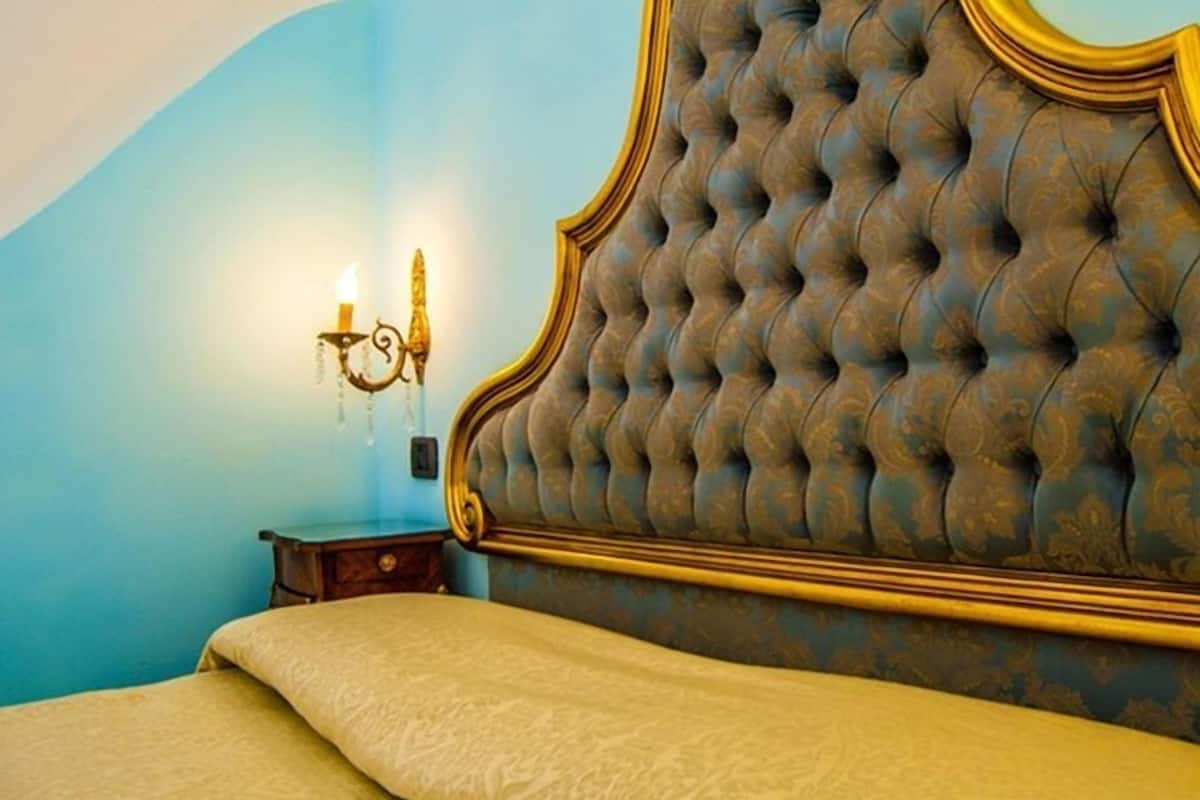 A bedroom with a tufted headboard, a bedside table, and a wall-mounted lamp.