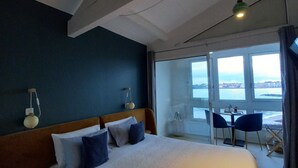A bedroom with a large bed, a view of the sea through a sliding door, and a table with chairs outside. - La Caravelle (Ciboure)