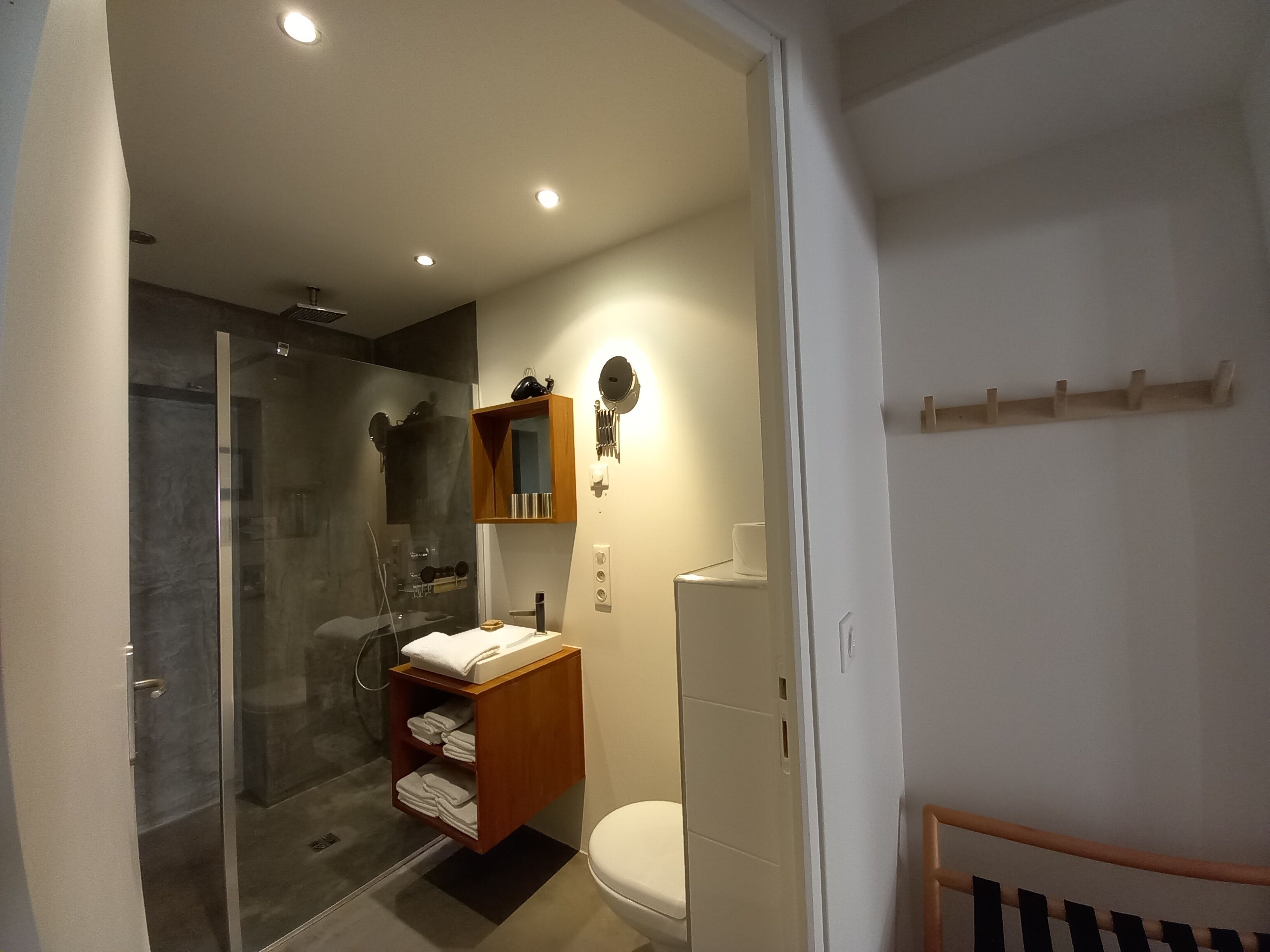 Un baño moderno con cabina de ducha de vidrio, tocador de madera con espejo y un inodoro.