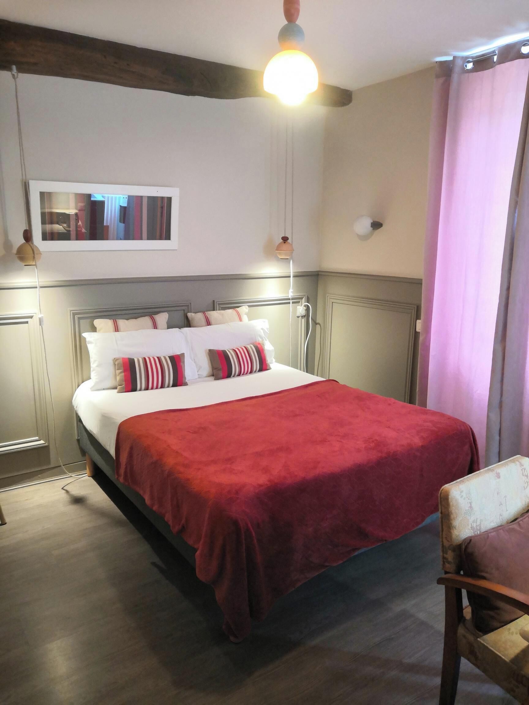 A neatly made bed with a red blanket, a wooden headboard, and a bedside lamp.