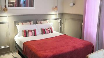 A neatly made bed with a red blanket, a wooden headboard, and a bedside lamp.