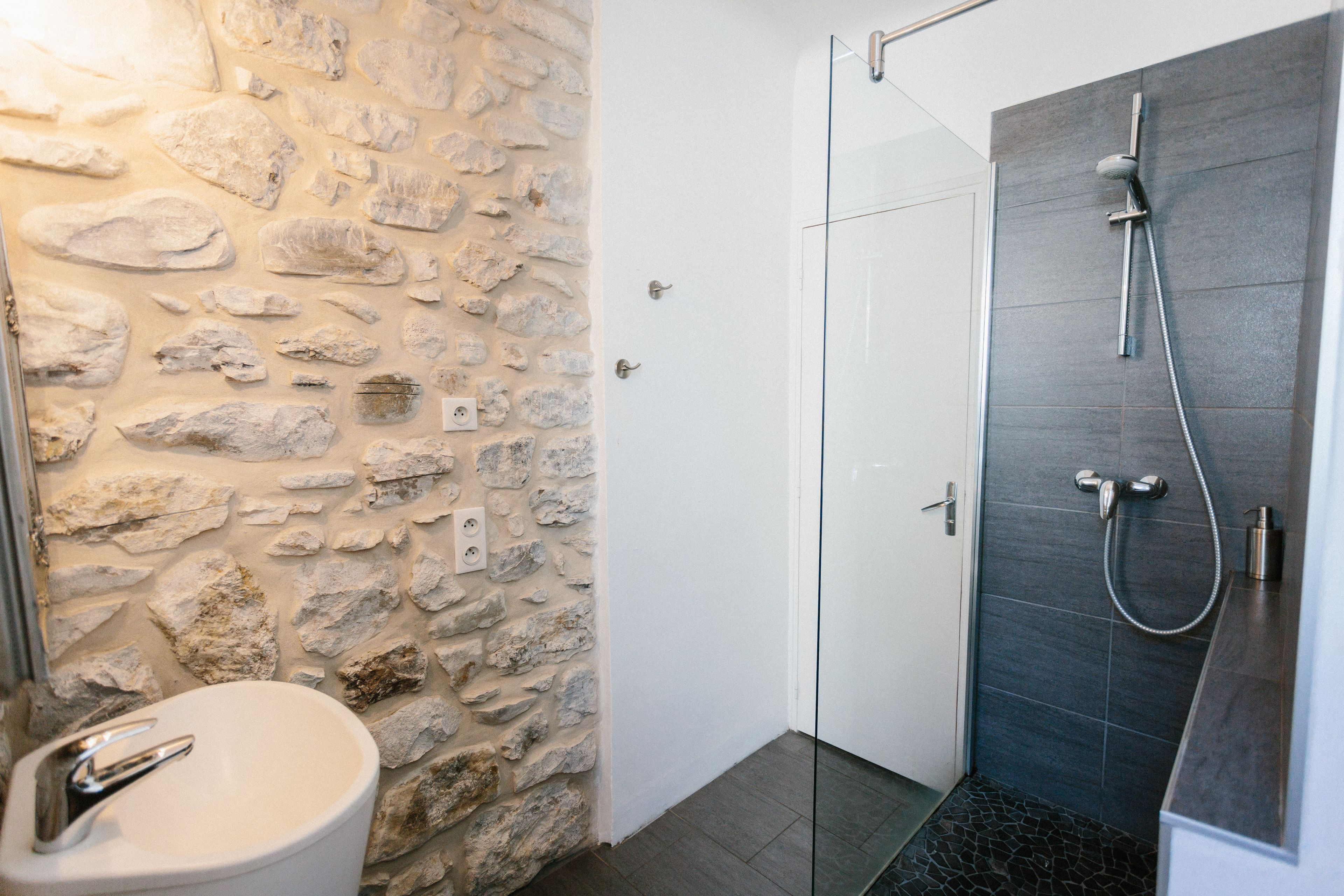A bathroom with a stone wall, a white sink, and a shower area.