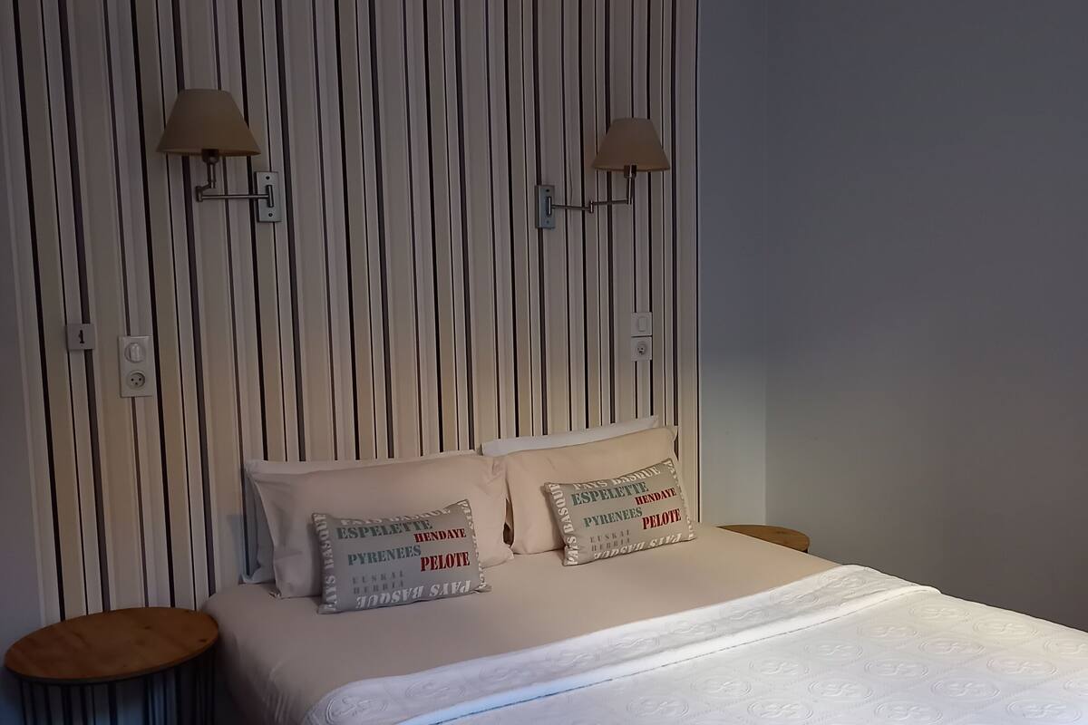 A neatly made bed with a white duvet, two bedside tables, a hanging lamp, and a striped wall.