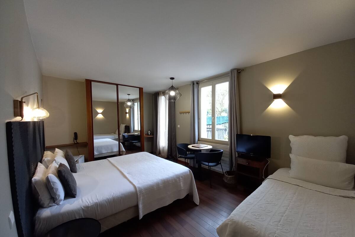 A hotel room with two beds, a desk, a chair, a TV, and a large mirror.