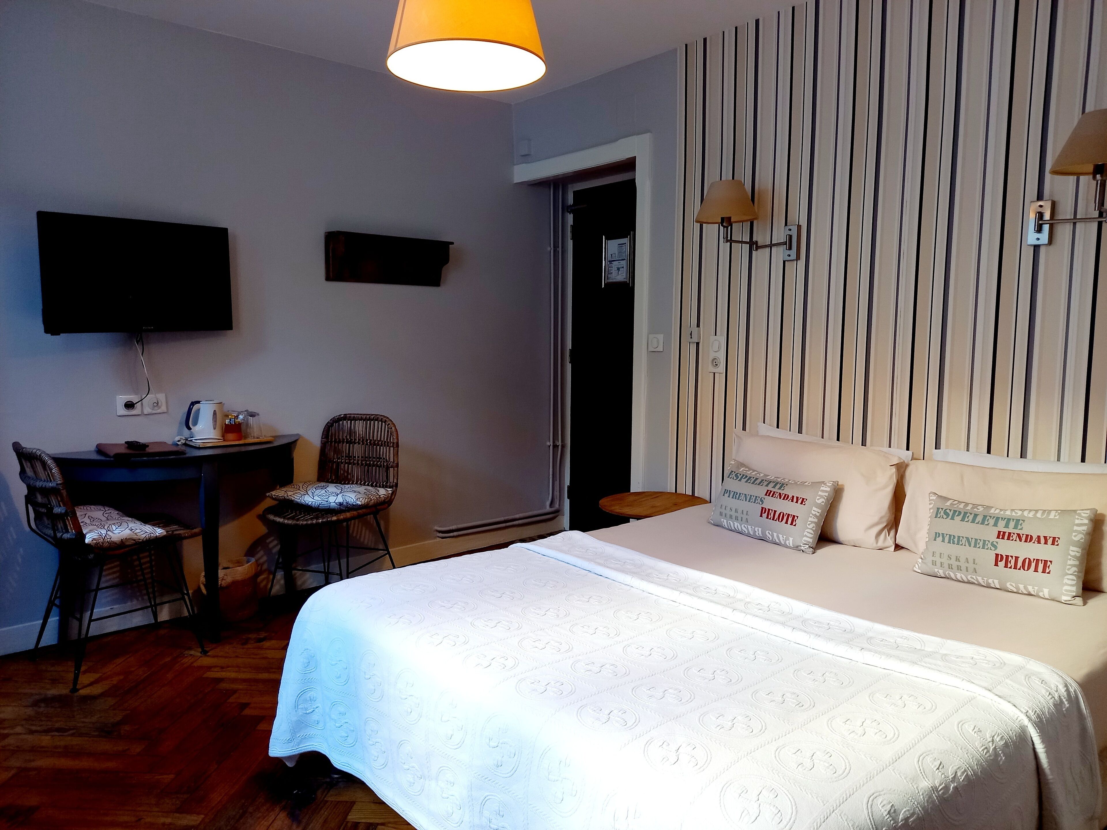 A hotel room with a bed, a desk with a chair, a television, and a wall with striped wallpaper.