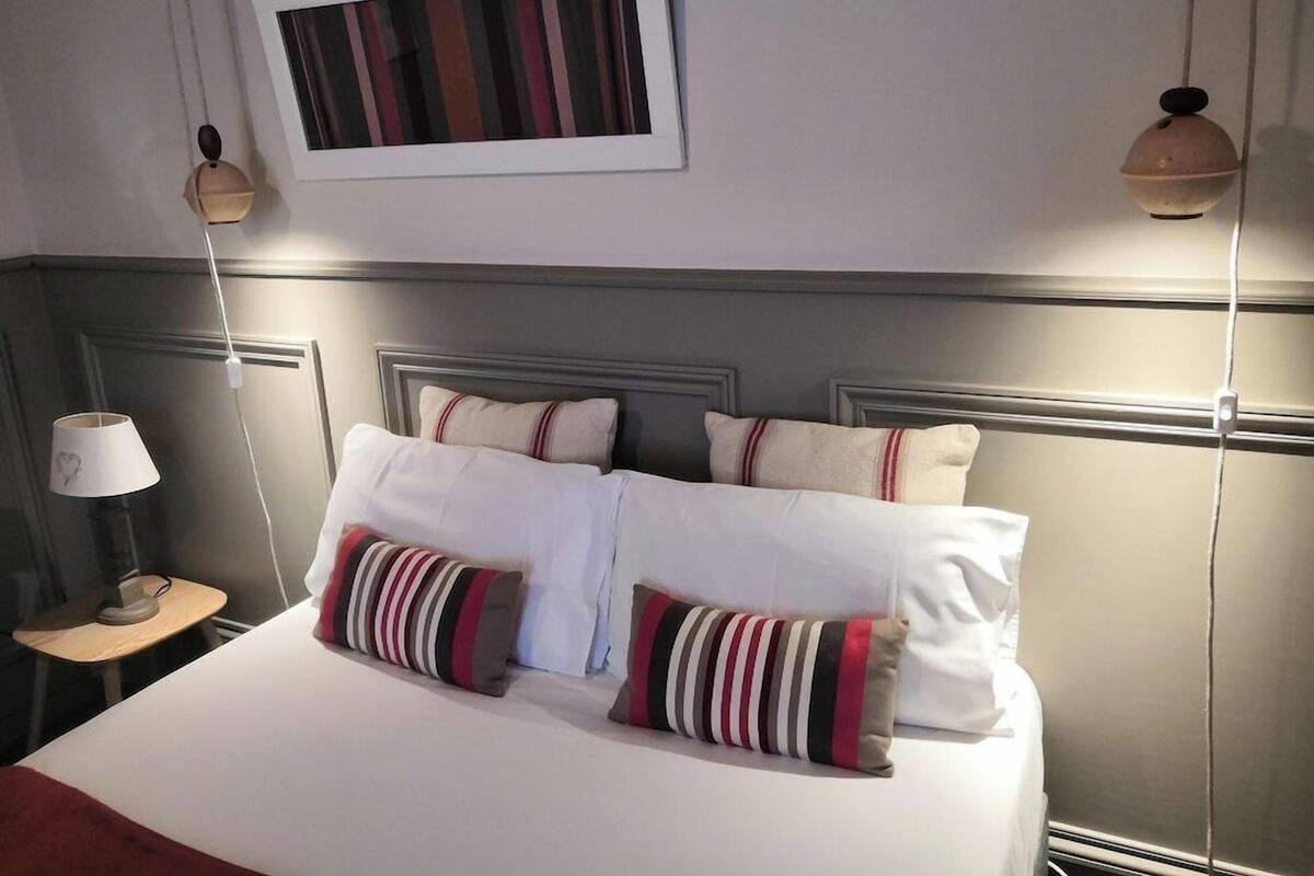 A hotel room with a bed, pillows, a bedside table with a lamp, and a wall-mounted picture.