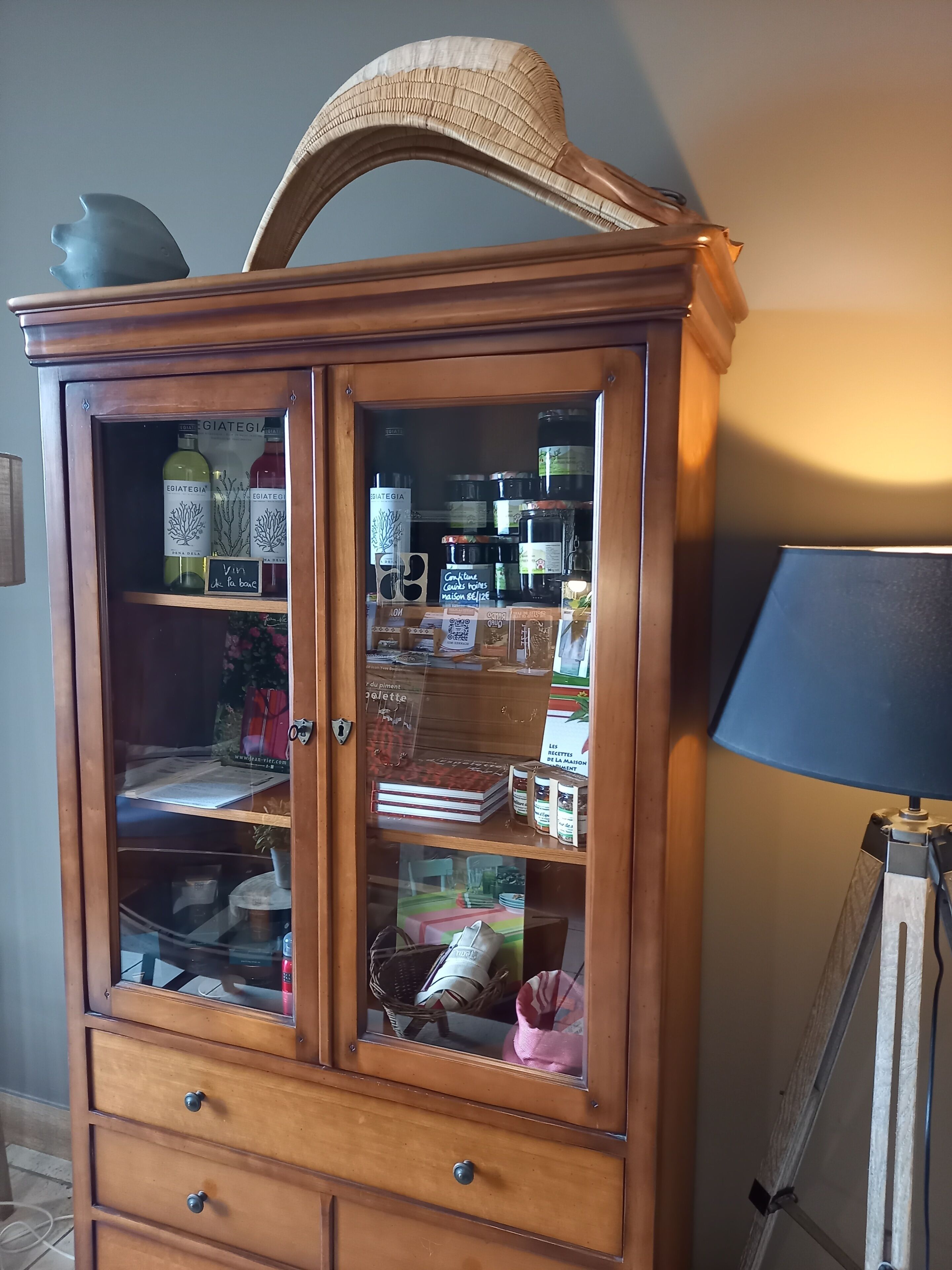 A wooden cabinet with glass doors containing various items like bottles, books, and jars.
