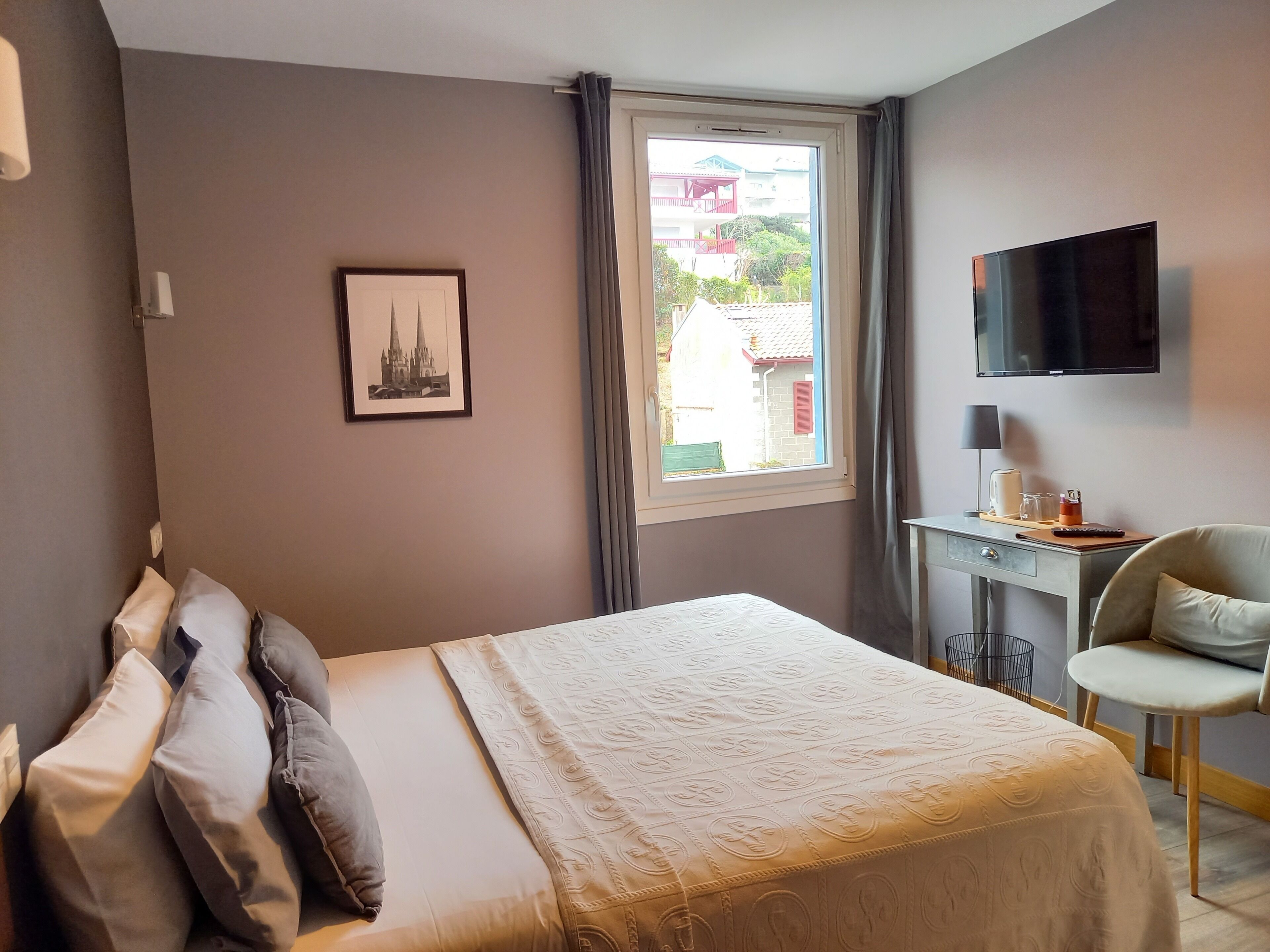 Ein Hotelzimmer mit Bett, Schreibtisch, Stuhl, Fernseher und einem Fenster mit Vorhängen.