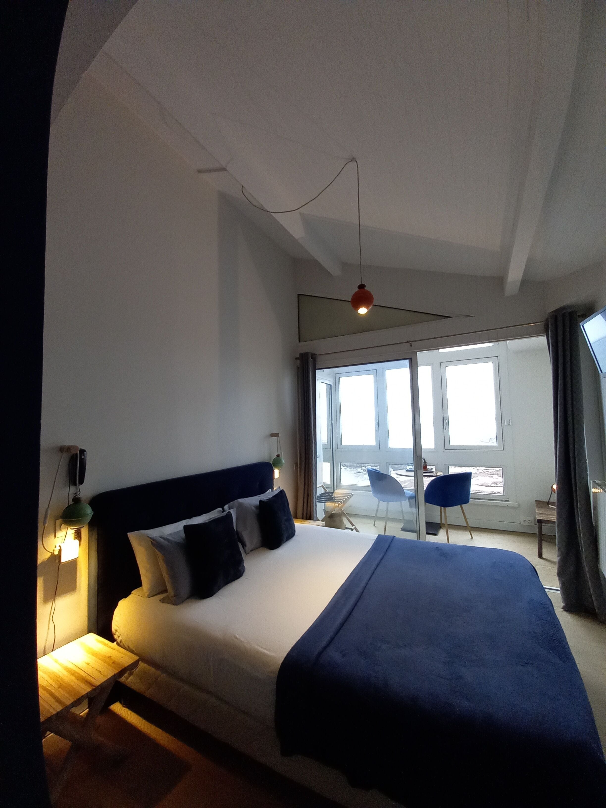 A hotel room with a large bed, a desk, a chair, and a view of the outdoors through a large window.