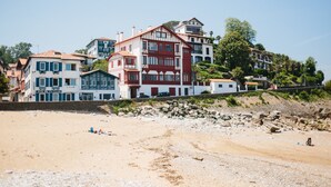 A coastal hotel with multiple buildings, a sandy beach, and rocky terrain. - La Caravelle (Ciboure)