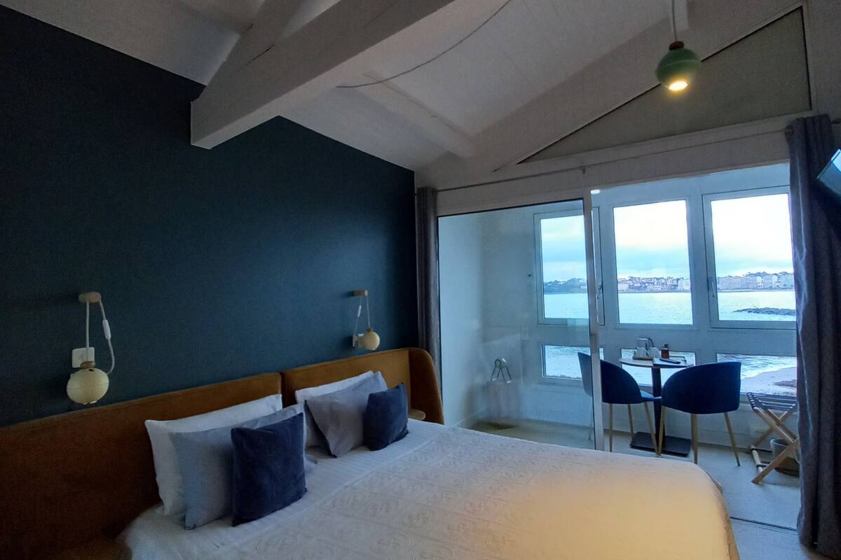 A hotel room with a large bed, a view of the sea, and a balcony with seating.