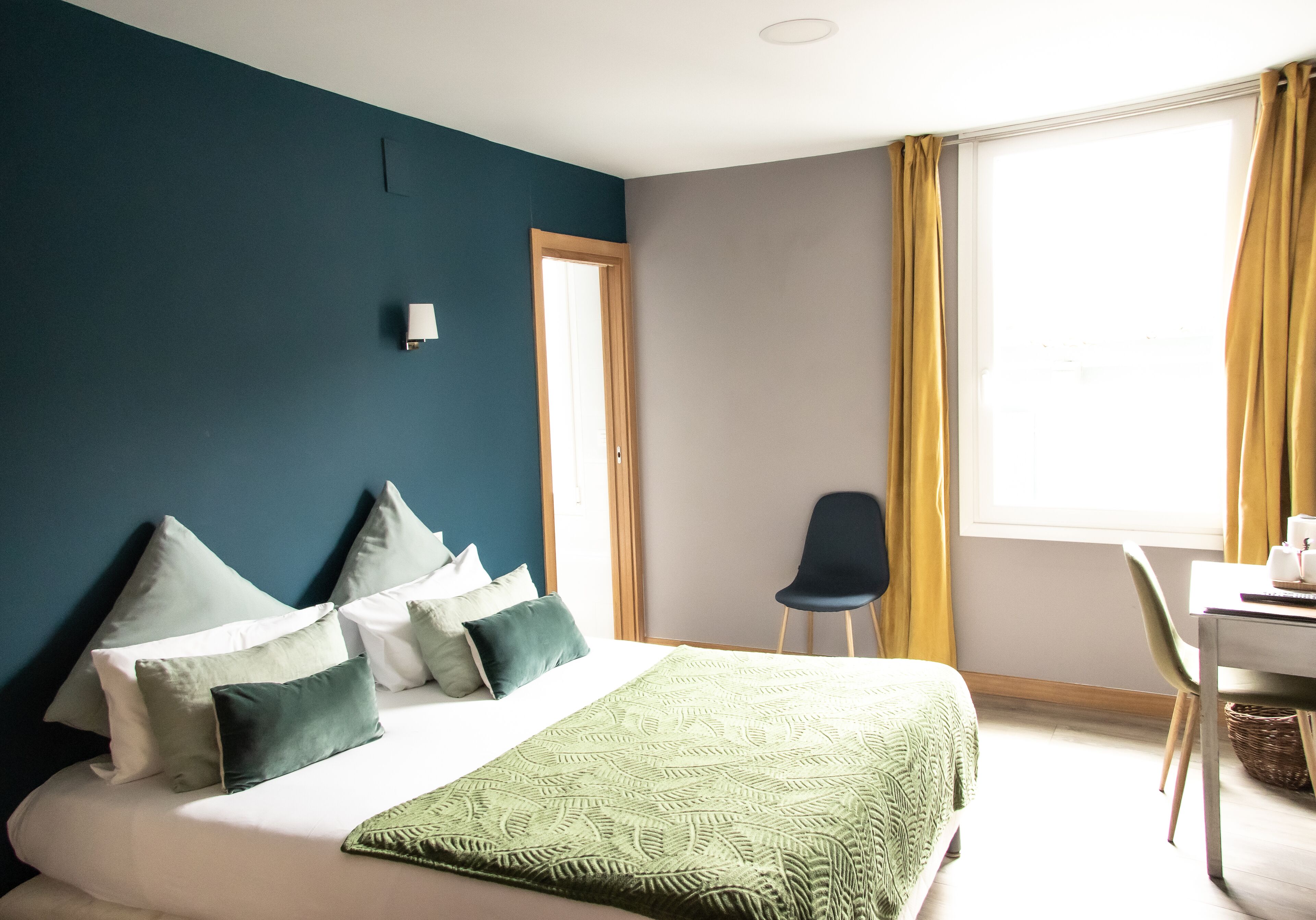 A hotel room with a bed, a desk, a chair, and a window with curtains.