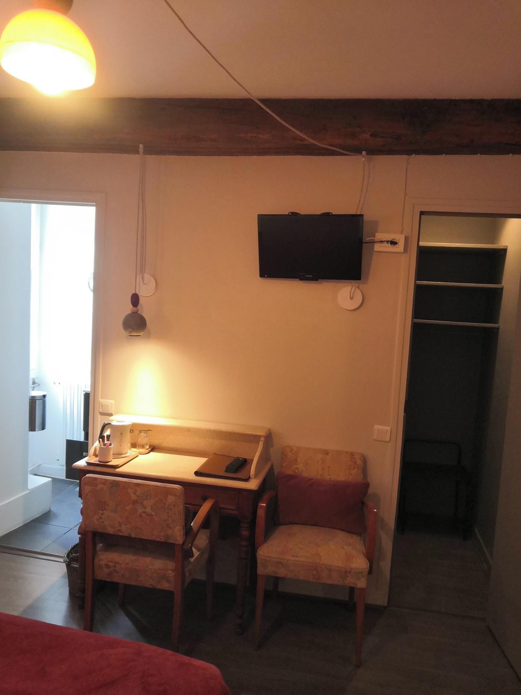Een kamer met een bureau, twee stoelen, een aan de muur bevestigde televisie en een kledingkast.