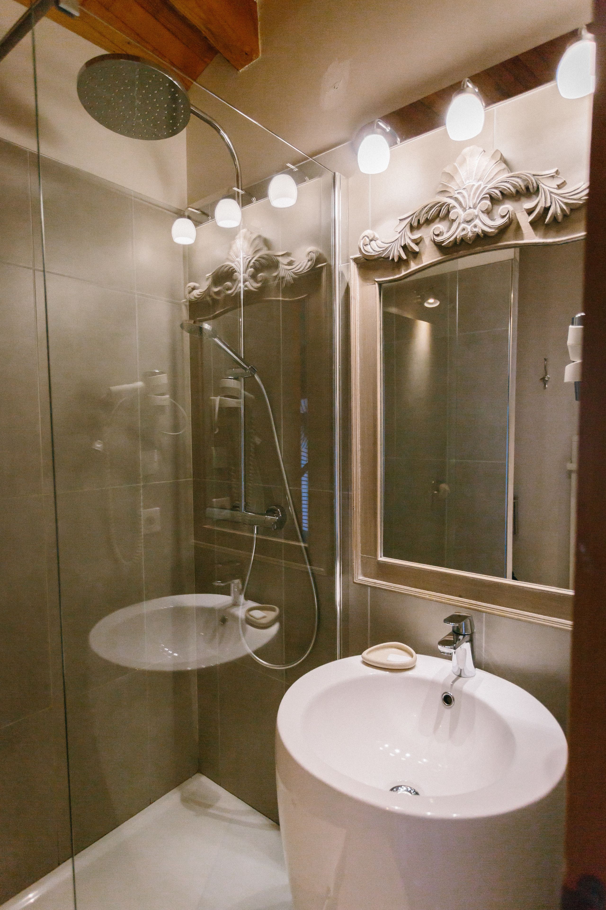 Een badkamer met een douche met glazen wand, een wit wastafelmeubel en een spiegel met decoratieve omlijsting.