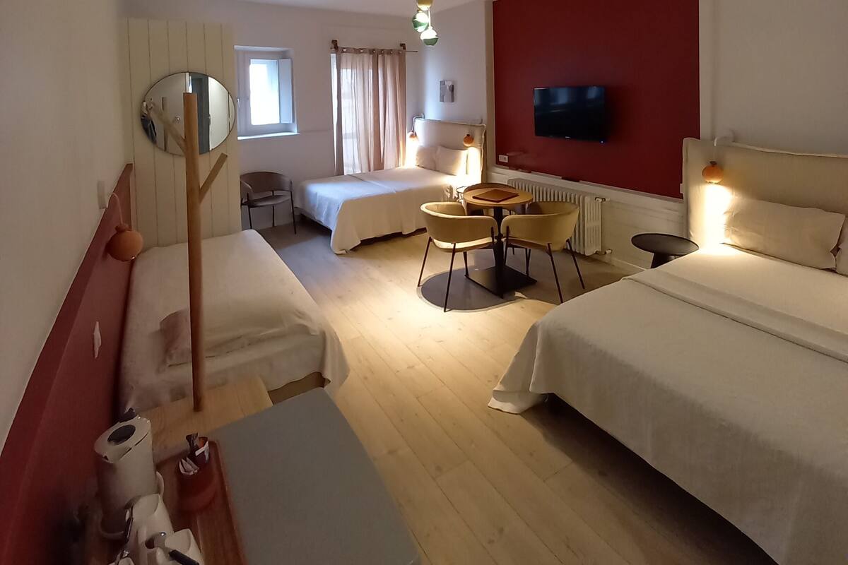 A hotel room with two beds, a small table with chairs, a TV mounted on the wall, and a window with curtains.