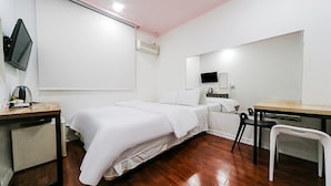 A hotel room with a bed, a desk, a chair, a TV, and an air conditioning unit. - Ace Motel (Gangneung)