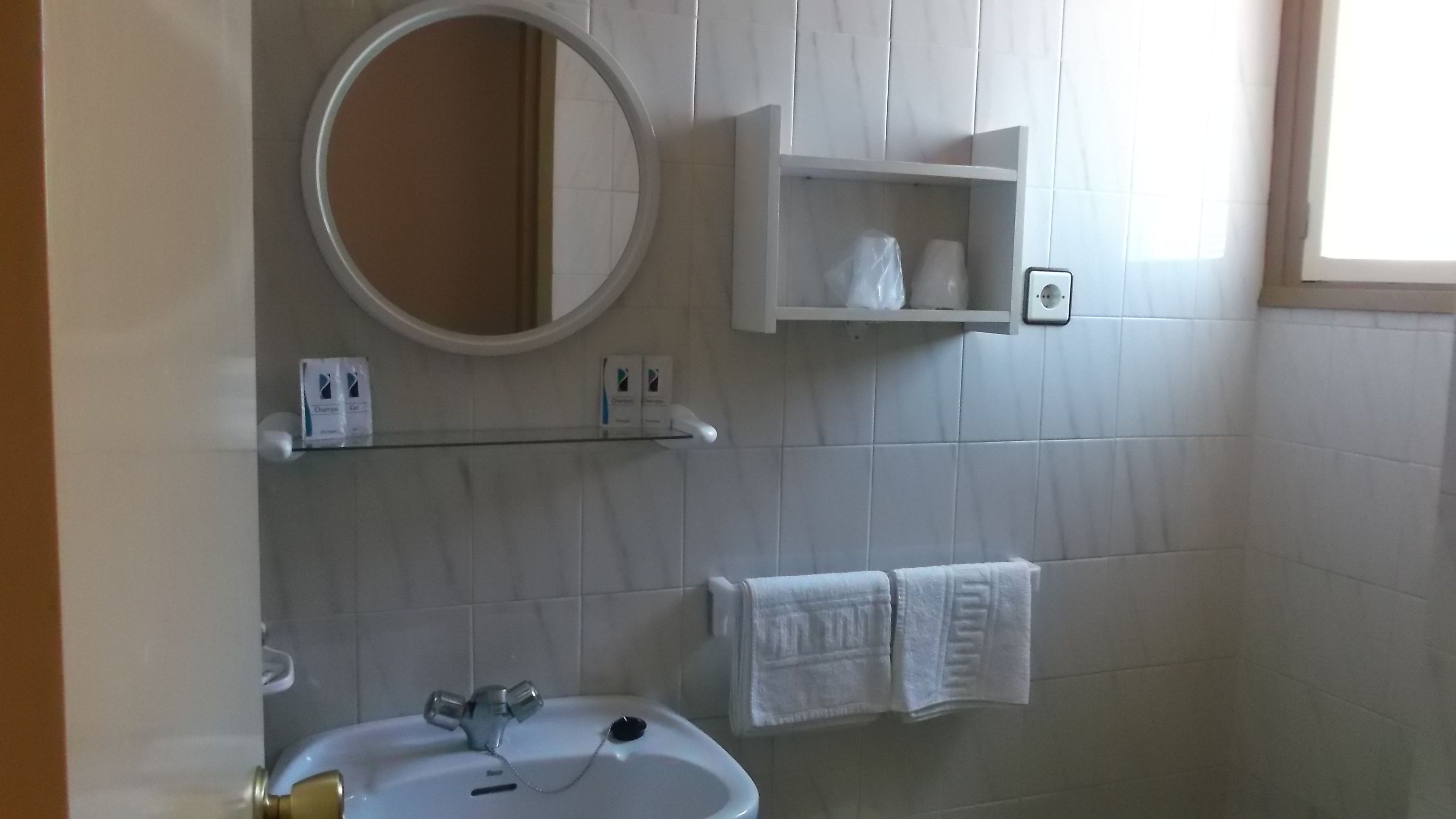 Un baño con un lavamanos blanco, un espejo y un perchero para toallas.