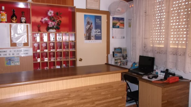 En reception med træbordplade, en opslagstavle med forskellige meddelelser, en kalender og en bærbar computer på bordet.