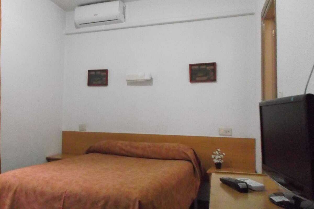 A small, simple room with a bed, a TV, and a small table.