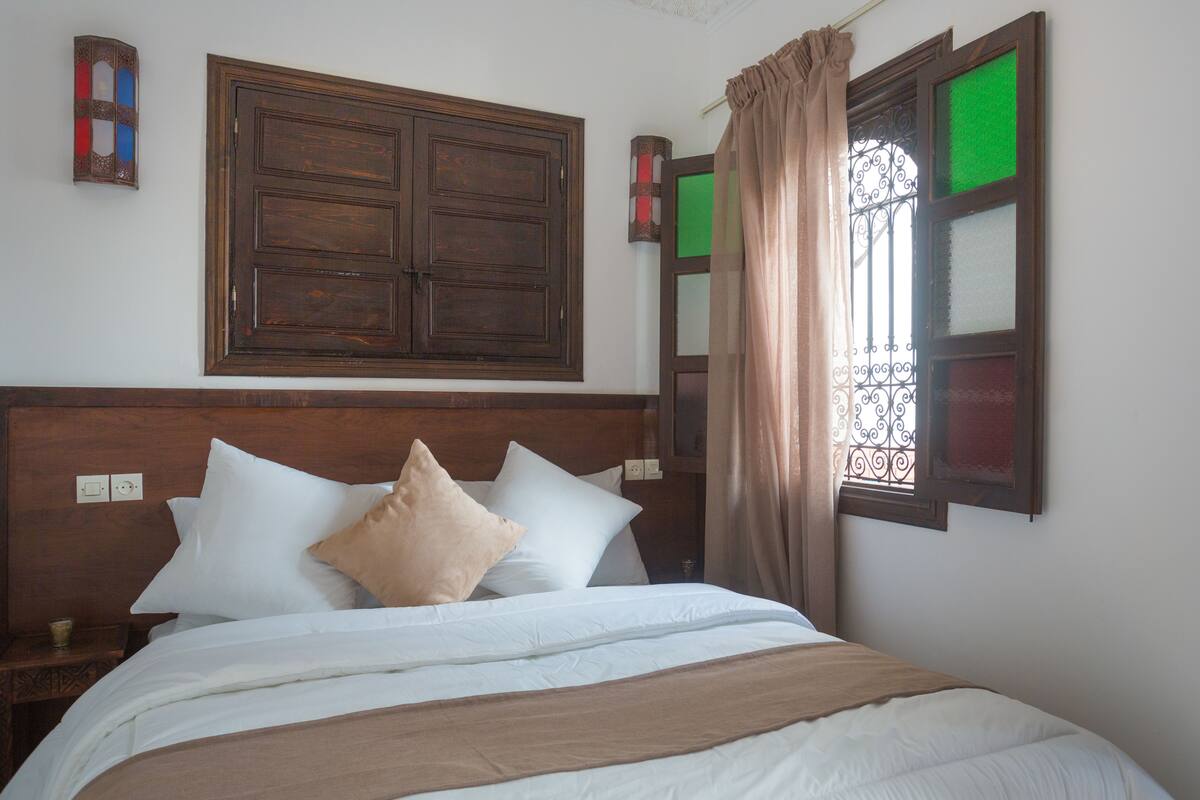 Una cama bien hecha con ropa de cama blanca y beige, un cabecero de madera y una puerta de madera grande encima.