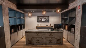 A reception area with a central counter, wooden flooring, and a sign reading "HOTEL DE ST. JOAN". - Hotelet de Sant Joan (Sant Joan de Les Abadesses)