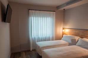 A hotel room with two beds, a wooden headboard, a mounted TV, and a window with sheer curtains. - Hotelet de Sant Joan (Sant Joan de Les Abadesses)