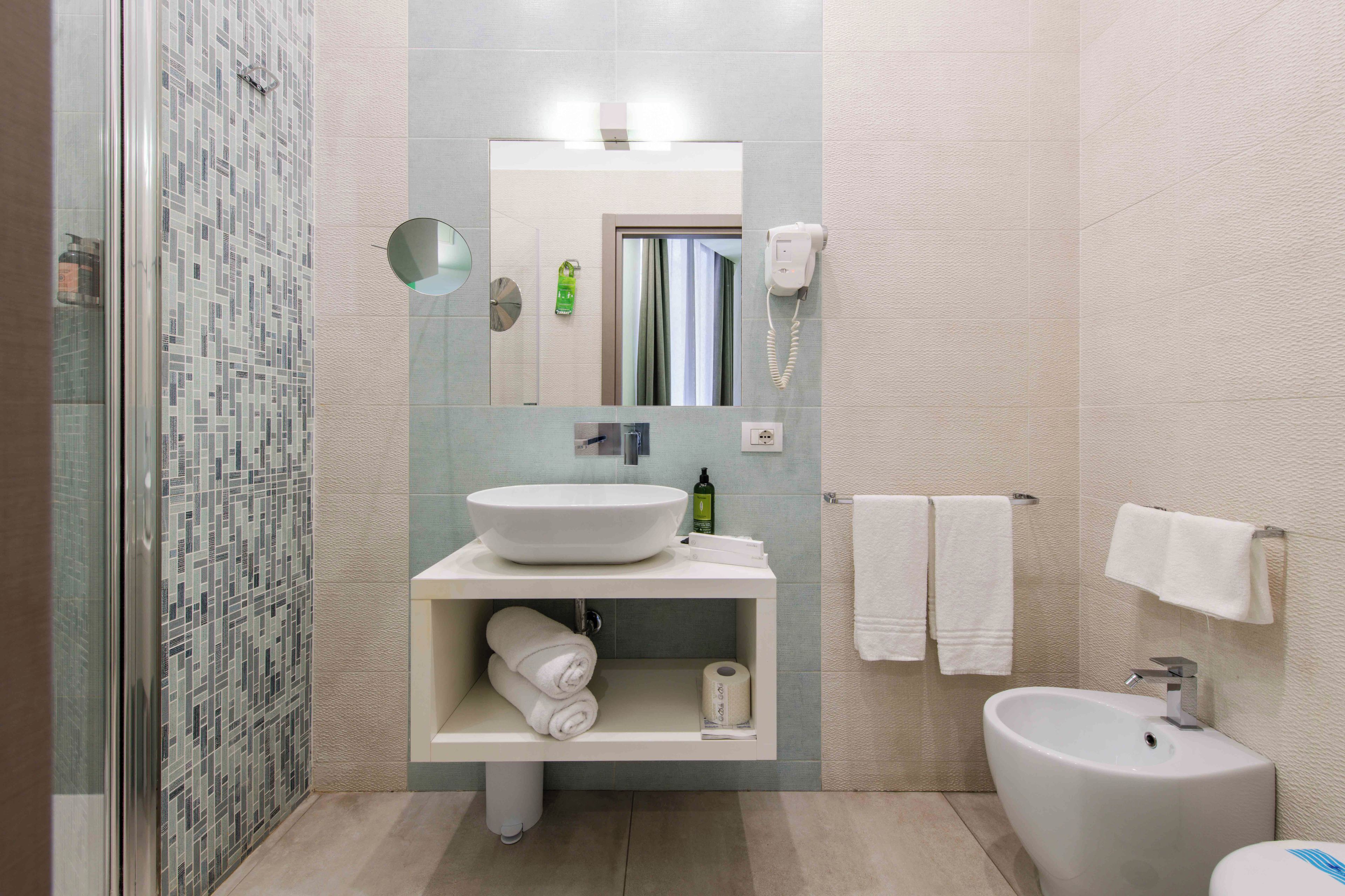 A modern bathroom with a glass-enclosed shower, a white sink, a bidet, and a towel rack.